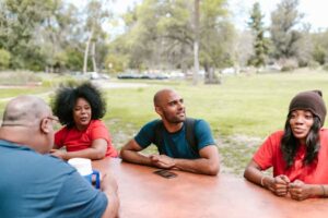 A diverse group of adults enjoying a casual outdoor gathering in a sunny park setting.